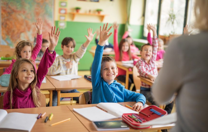 School children raising their hands ready to answer the question. Large group of school children raising their hands ready to answer the question.